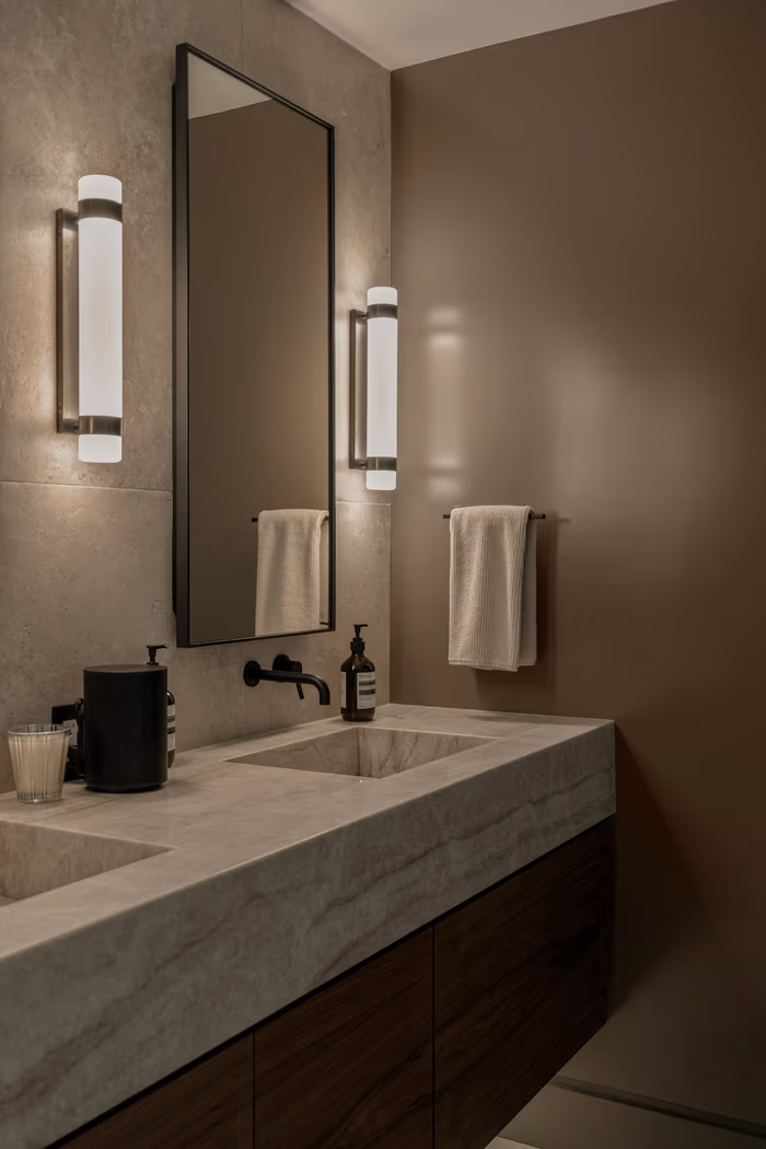 Bathroom vanity with tall slim sconces mounted on either side of a mirror at roughly face height