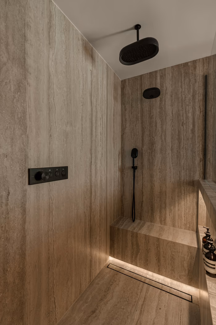 Walk-in shower lined in large-format stone-look tile, with a built-in bench and a linear drain set along the floor